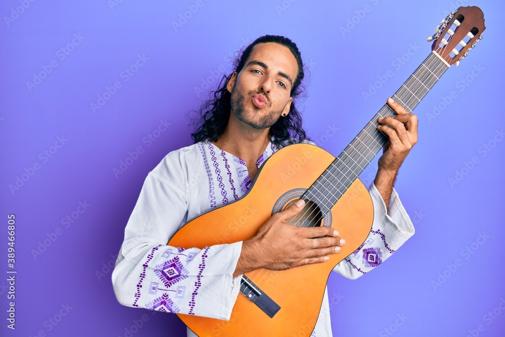 Young handsome man with long hair playing classical guitar looking at the camera blowing a kiss being lovely and sexy. love expression. Young handsome man with long hair playing classical guitar looking at the camera blowing a kiss being lovely and sexy. love expression.