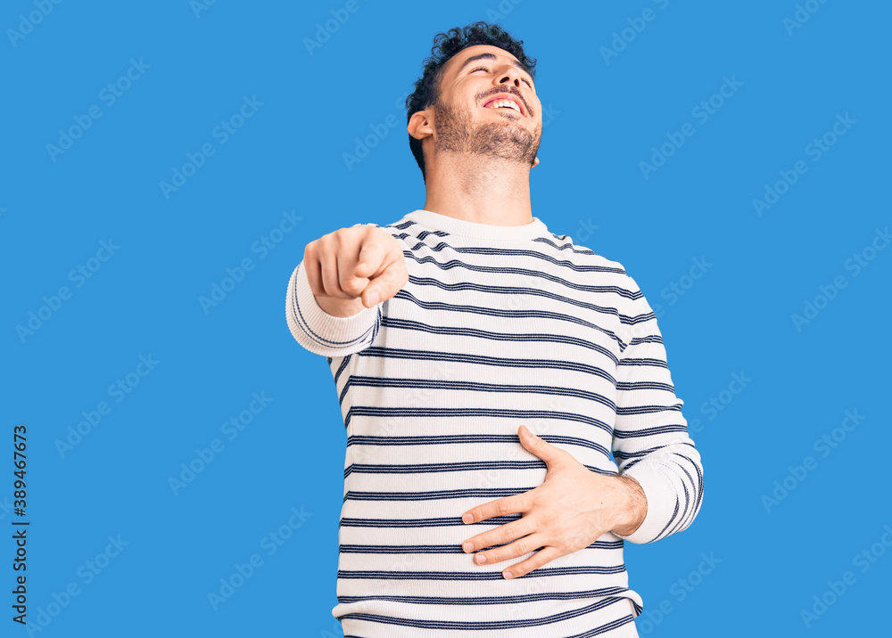 Fototapeta premium Young hispanic man wearing casual clothes laughing at you, pointing finger to the camera with hand over body, shame expression