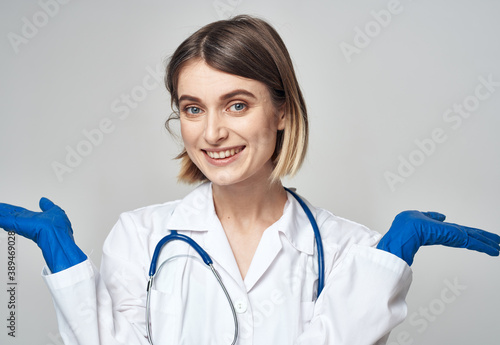 A nurse in a medical gown and blue gloves gestures with a stethoscope around her neck