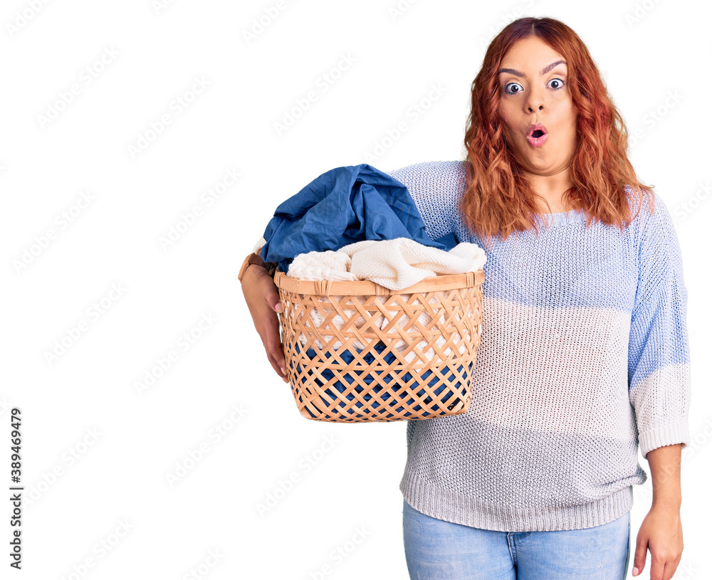 Young latin woman holding laundry basket scared and amazed with open mouth for surprise, disbelief face Young latin woman holding laundry basket scared and amazed with open mouth for surprise, disbelief face