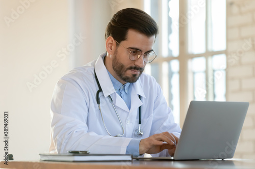 Advancing in skills. Inspired concentrated millennial doctor intern qualified specialist using computer to read medical literature online, asking questions on professional forums to specify diagnosis
