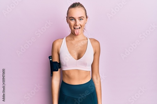 Beautiful blonde woman wearing sportswear and arm band sticking tongue out happy with funny expression. emotion concept. © Krakenimages.com