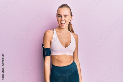 Beautiful blonde woman wearing sportswear and arm band winking looking at the camera with sexy expression, cheerful and happy face. © Krakenimages.com