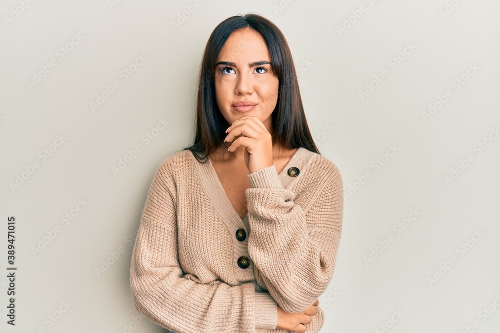 Young beautiful hispanic girl wearing casual winter sweater thinking concentrated about doubt with finger on chin and looking up wondering Young beautiful hispanic girl wearing casual winter sweater thinking concentrated about doubt with finger on chin and looking up wondering