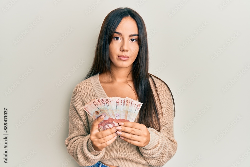 Young beautiful hispanic girl holding 10 colombian pesos banknotes relaxed with serious expression on face. simple and natural looking at the camera. Young beautiful hispanic girl holding 10 colombian pesos banknotes relaxed with serious expression on face. simple and natural looking at the camera.