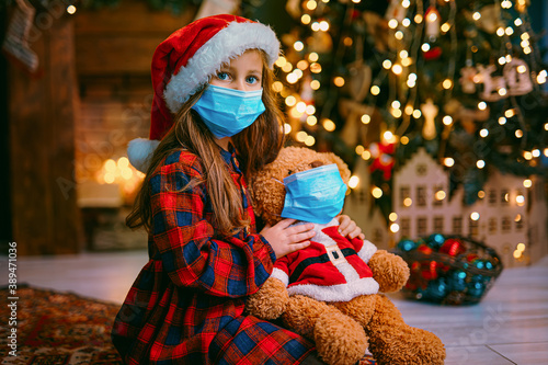 Portrait of cutel little child girl in medical mask playing with Taddy bear, New year holiday concept. Covid-19 concept.