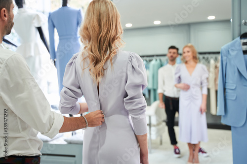 Woman looking at the mirror while stylist buttoning the dress