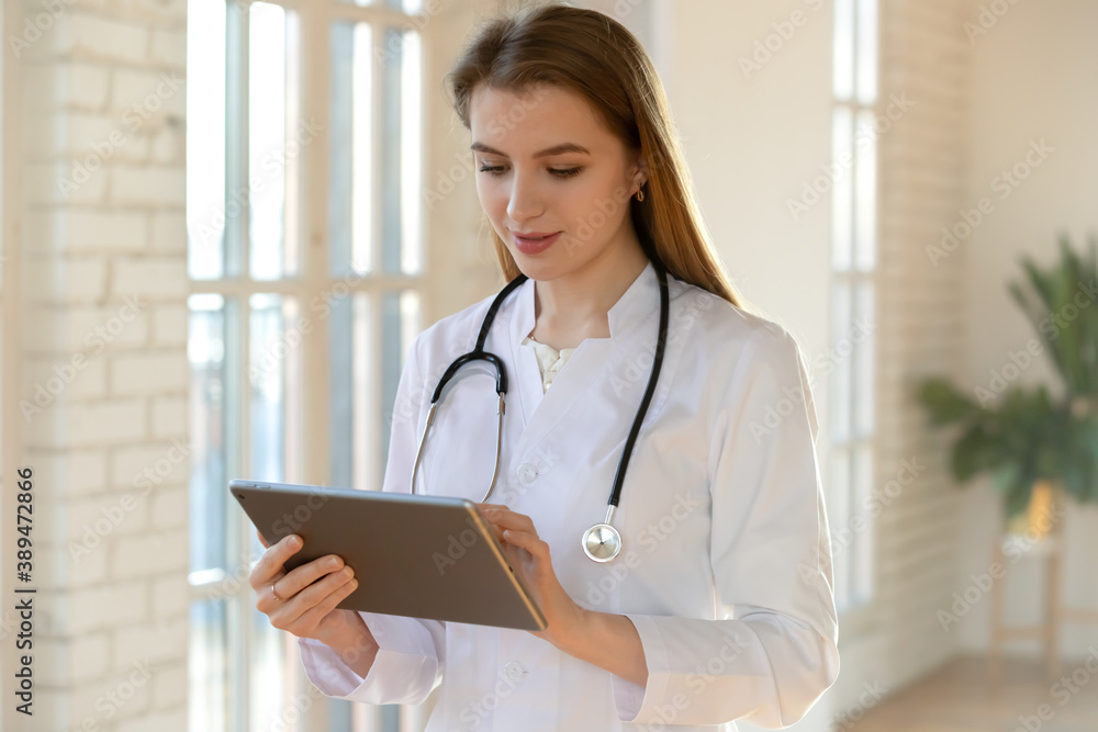 Electronic paperwork. Thoughtful millennial female doctor admitting physician in hospital filling in anamnesis details in medical history files online, making records of patient round results on pad Electronic paperwork. Thoughtful millennial female doctor admitting physician in hospital filling in anamnesis details in medical history files online, making records of patient round results on pad