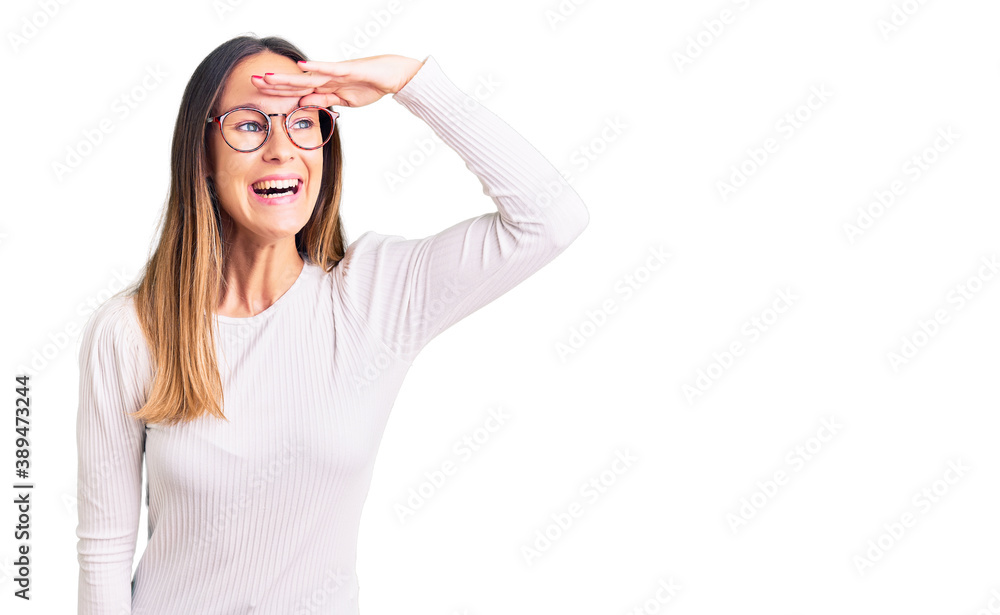 Beautiful brunette young woman wearing casual white sweater and glasses very happy and smiling looking far away with hand over head. searching concept. Beautiful brunette young woman wearing casual white sweater and glasses very happy and smiling looking far away with hand over head. searching concept.
