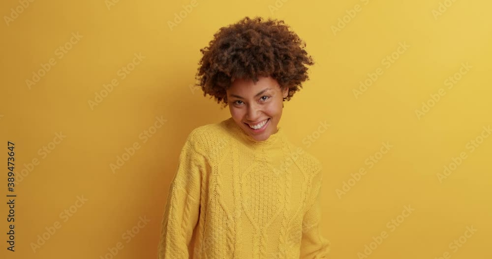Optimistic joyous young woman with Afro hair dances carefree and raises arms dressed in casual clothing celebrates something spends free time on disco party isolated over yellow studio background Optimistic joyous young woman with Afro hair dances carefree and raises arms dressed in casual clothing celebrates something spends free time on disco party isolated over yellow studio background