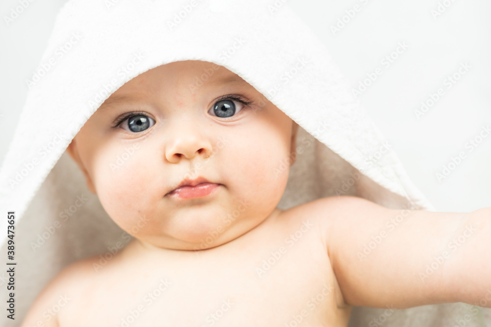 Cute caucasian baby with blue eyes covered with white bath towel on white background. Portrait of tiny naked baby boy looking to the camera.