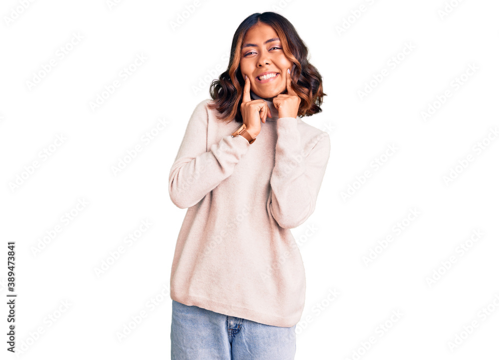 Young beautiful mixed race woman wearing winter turtleneck sweater smiling with open mouth, fingers pointing and forcing cheerful smile Young beautiful mixed race woman wearing winter turtleneck sweater smiling with open mouth, fingers pointing and forcing cheerful smile