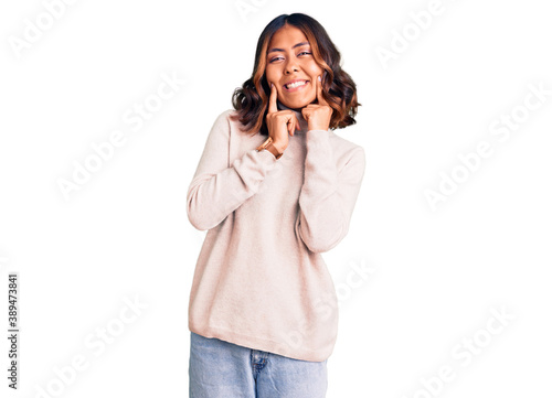 Young beautiful mixed race woman wearing winter turtleneck sweater smiling with open mouth, fingers pointing and forcing cheerful smile © Krakenimages.com