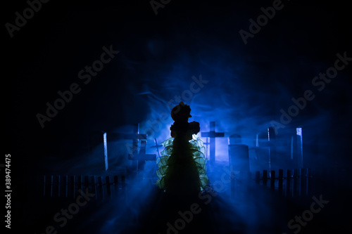 Girl walking alone in the cemetery at night. Dark toned foggy background. Horror Halloween concept