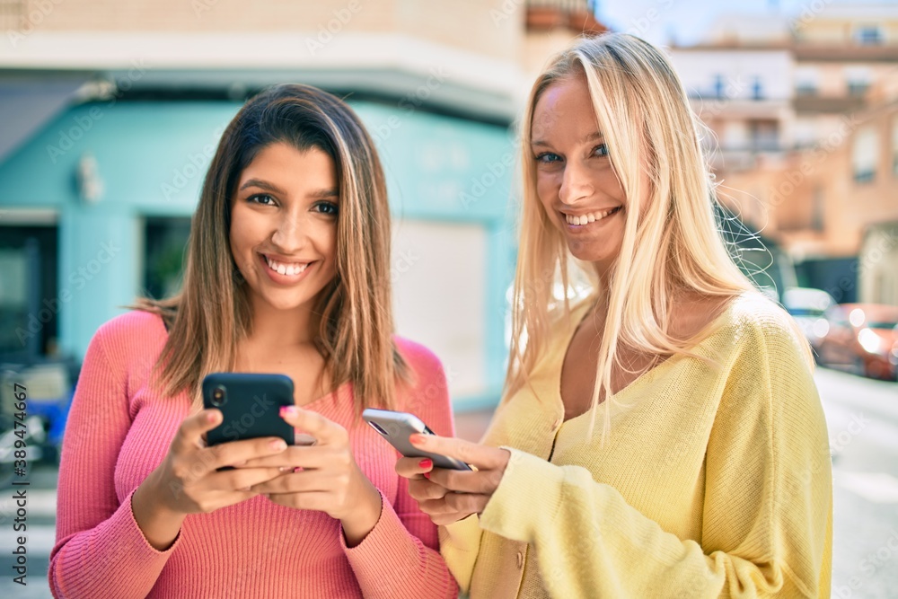 Two beautiful and young girl friends together having fun at the city using smartphone Two beautiful and young girl friends together having fun at the city using smartphone