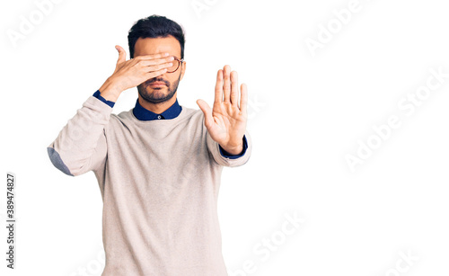 Young handsome hispanic man wearing elegant clothes and glasses covering eyes with hands and doing stop gesture with sad and fear expression. embarrassed and negative concept.