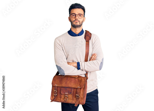 Young handsome hispanic man wearing leather bag skeptic and nervous, disapproving expression on face with crossed arms. negative person.