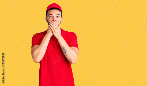 Young handsome hispanic man wearing delivery courier uniform shocked covering mouth with hands for mistake. secret concept.