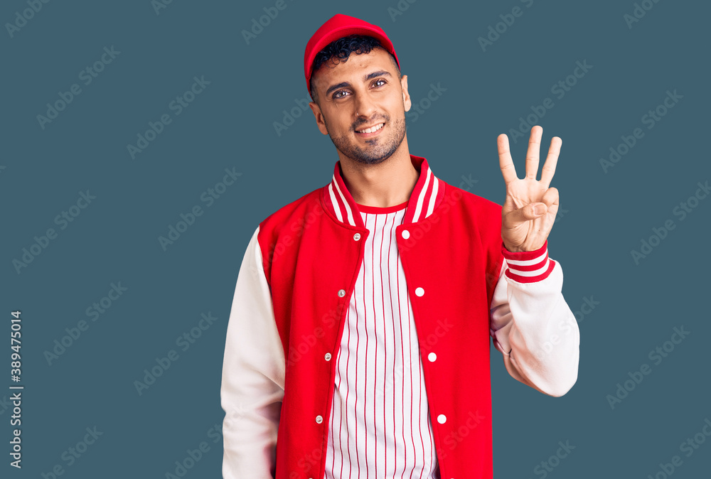 Fototapeta premium Young hispanic man wearing baseball uniform showing and pointing up with fingers number three while smiling confident and happy.