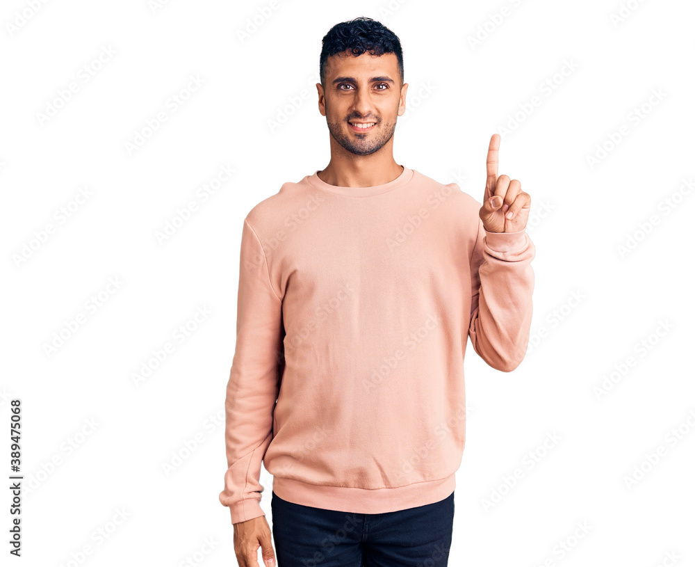 Young hispanic man wearing casual clothes showing and pointing up with finger number one while smiling confident and happy. Young hispanic man wearing casual clothes showing and pointing up with finger number one while smiling confident and happy.