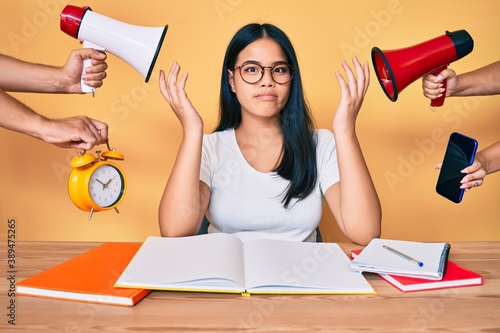 Young beautiful asian girl stuying for university getting stressed out clueless and confused with open arms, no idea and doubtful face. photo