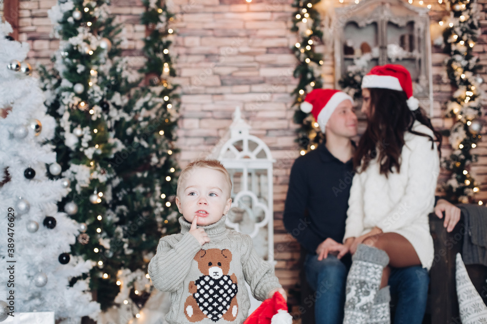 Child holding his finger close to mouth while his loving parents sitting by the Christmas tree