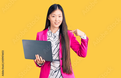 Young beautiful chinese woman using laptop pointing finger to one self smiling happy and proud