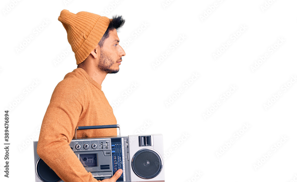 Handsome latin american young man holding boombox, listening to music looking to side, relax profile pose with natural face and confident smile.