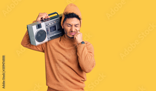 Handsome latin american young man holding boombox, listening to music touching mouth with hand with painful expression because of toothache or dental illness on teeth. dentist concept.
