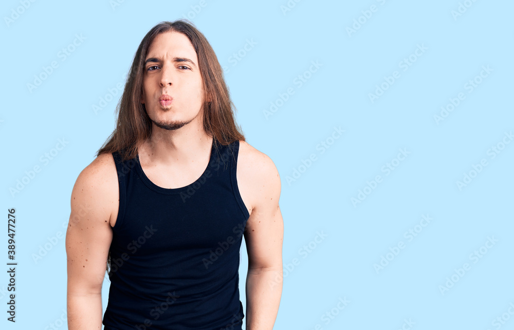 Young adult man with long hair wearing goth style with black clothes looking at the camera blowing a kiss on air being lovely and sexy. love expression. Young adult man with long hair wearing goth style with black clothes looking at the camera blowing a kiss on air being lovely and sexy. love expression.