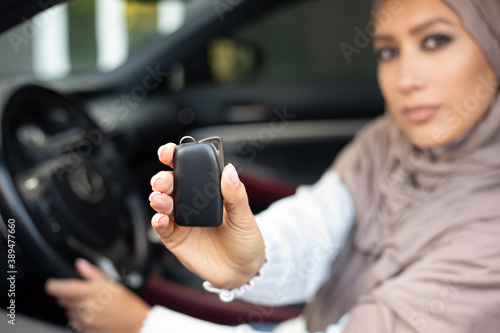 Young muslim lady showing auto key, sitting on driver's seat