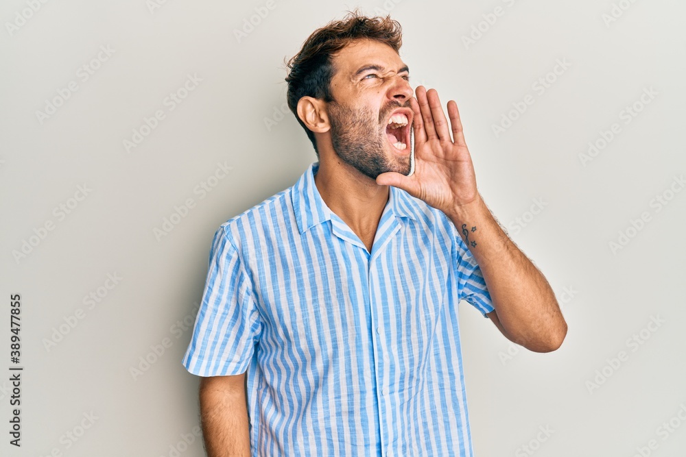 Handsome man with beard wearing casual shirt shouting and screaming loud to side with hand on mouth. communication concept.