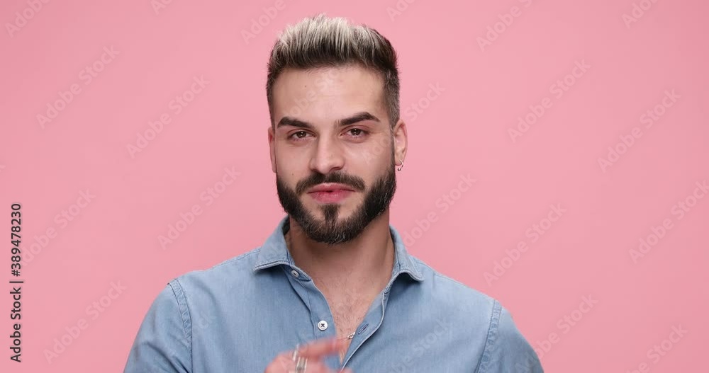 young casual man smiling at the camera and asking for silence against pink background young casual man smiling at the camera and asking for silence against pink background
