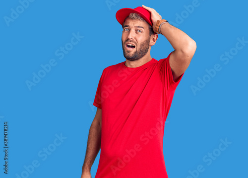 Young handsome blond man wearing t-shirt and cap surprised with hand on head for mistake, remember error. forgot, bad memory concept.