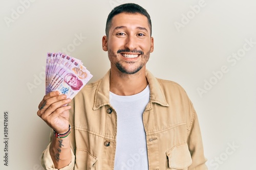 Photography Handsome man with tattoos holding 50 mexican pesos banknotes looking positive an