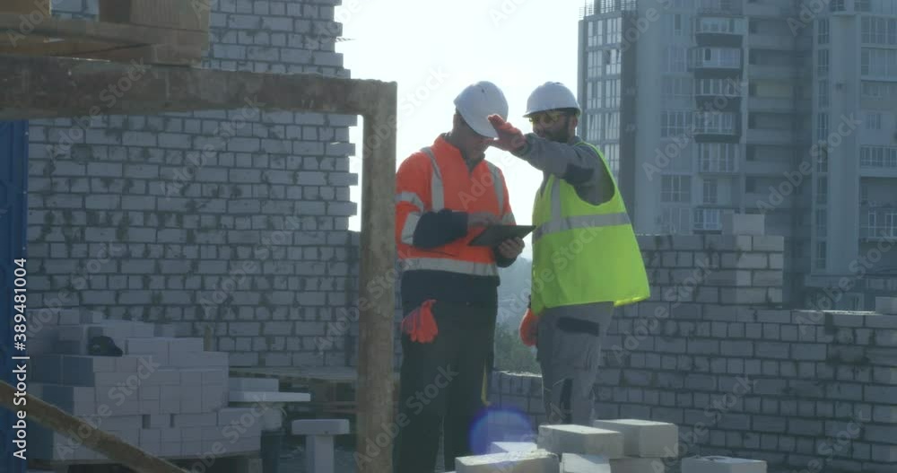 Builders with tablet examining unfinished brick building Builders with tablet examining unfinished brick building