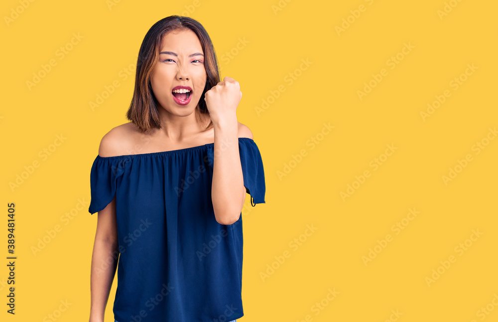 Young beautiful chinese girl wearing casual clothes angry and mad raising fist frustrated and furious while shouting with anger. rage and aggressive concept. Young beautiful chinese girl wearing casual clothes angry and mad raising fist frustrated and furious while shouting with anger. rage and aggressive concept.