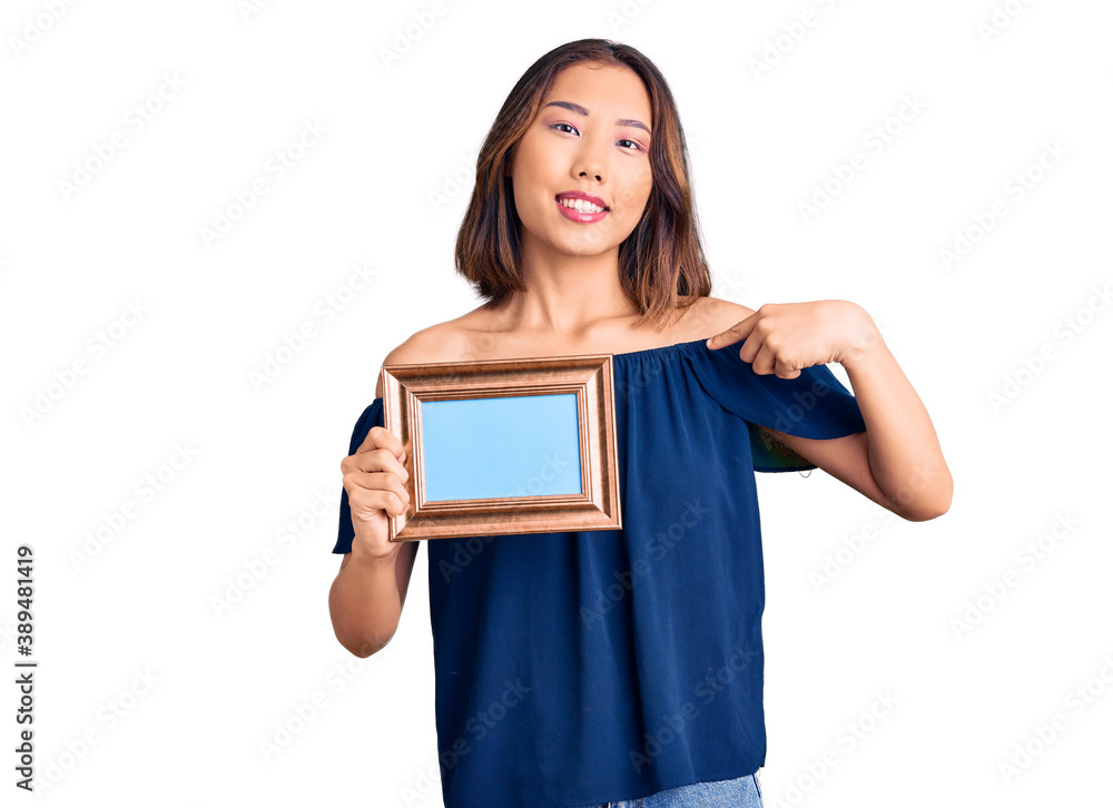 Young beautiful chinese girl holding empty frame pointing finger to one self smiling happy and proud Young beautiful chinese girl holding empty frame pointing finger to one self smiling happy and proud