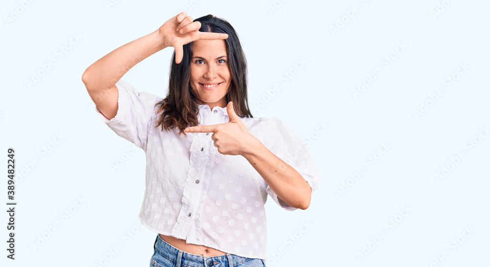 Young beautiful brunette woman wearing casual shirt smiling making frame with hands and fingers with happy face. creativity and photography concept. Young beautiful brunette woman wearing casual shirt smiling making frame with hands and fingers with happy face. creativity and photography concept.