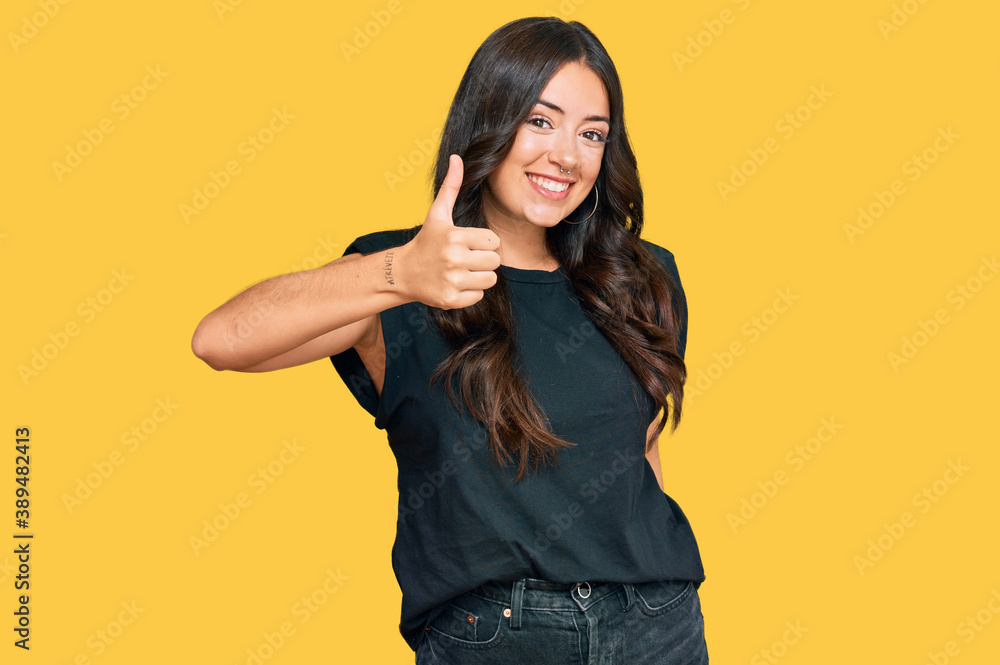 Beautiful brunette young woman wearing black shirt doing happy thumbs up gesture with hand. approving expression looking at the camera showing success. Beautiful brunette young woman wearing black shirt doing happy thumbs up gesture with hand. approving expression looking at the camera showing success.