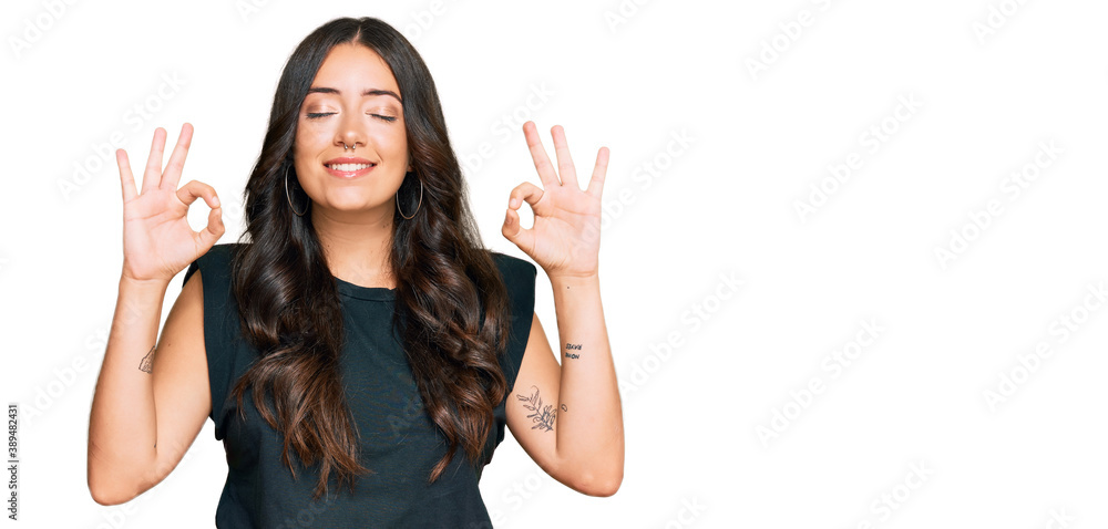 Beautiful brunette young woman wearing black shirt relax and smiling with eyes closed doing meditation gesture with fingers. yoga concept. Beautiful brunette young woman wearing black shirt relax and smiling with eyes closed doing meditation gesture with fingers. yoga concept.