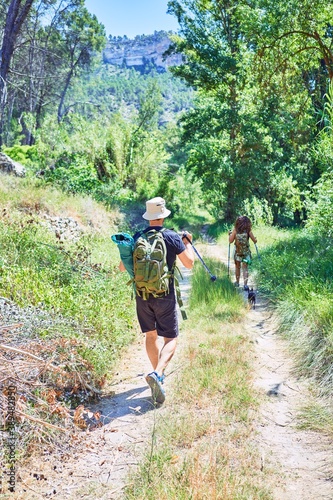 Beautiful couple of hiker on back view wearing backpack doing trekking using hiking stick at forest