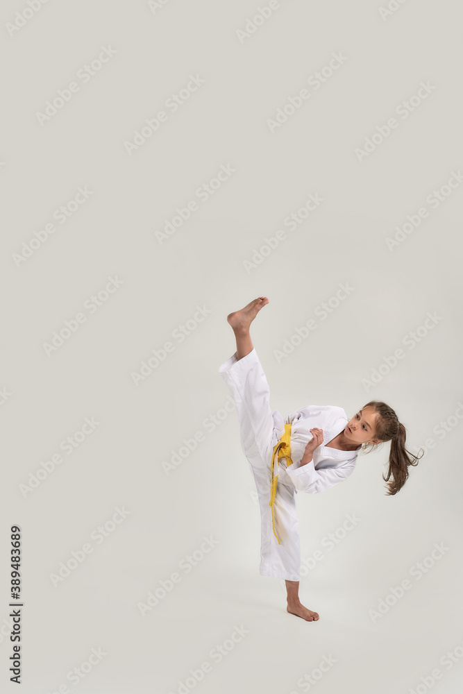 Naklejka premium Full length shot of little karate girl in white kimono with a yellow sash exercising and fighting, doing martial arts, standing isolated over white background