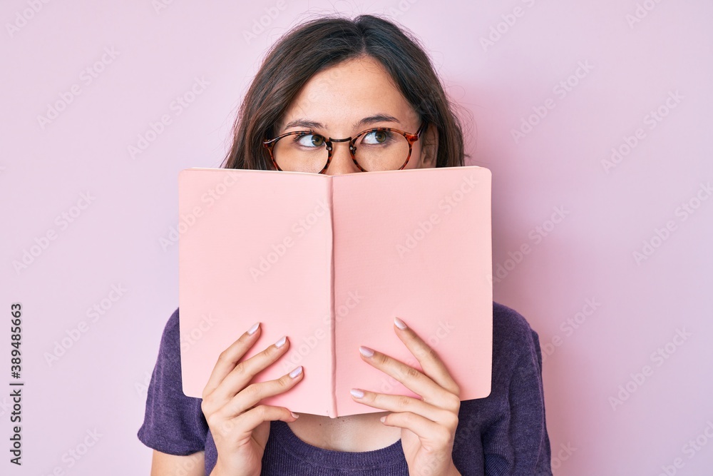 Young beautiful woman wearing glasses reading book smiling looking to the side and staring away thinking. Young beautiful woman wearing glasses reading book smiling looking to the side and staring away thinking.