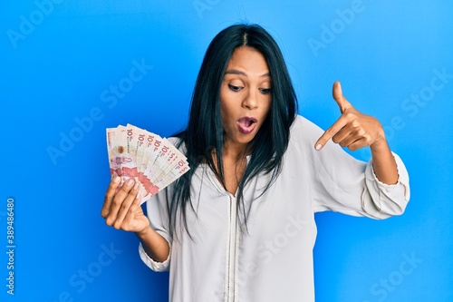 Young african american woman holding 10 colombian pesos banknotes pointing down with fingers showing advertisement, surprised face and open mouth