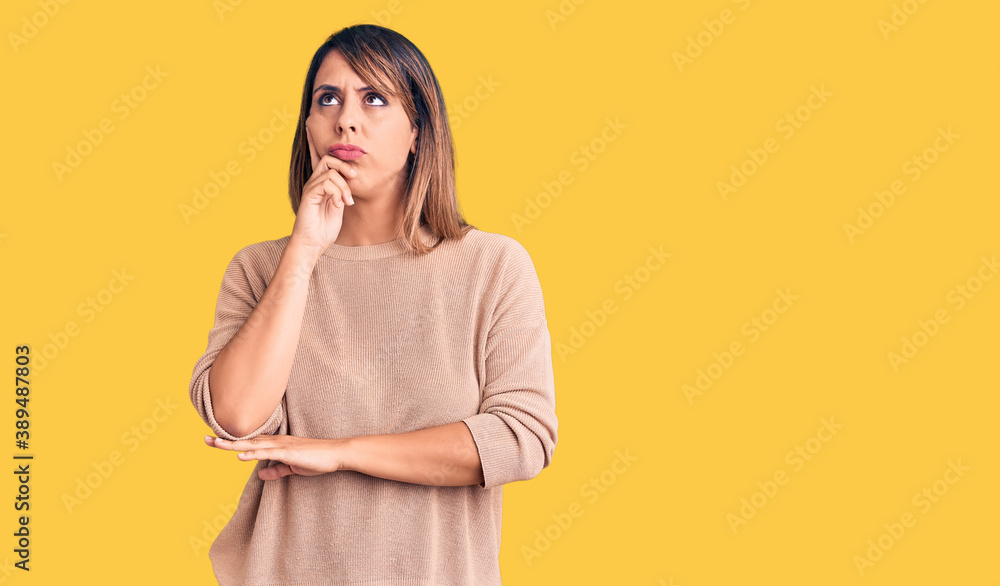 Young beautiful woman wearing casual sweater serious face thinking about question with hand on chin, thoughtful about confusing idea Young beautiful woman wearing casual sweater serious face thinking about question with hand on chin, thoughtful about confusing idea
