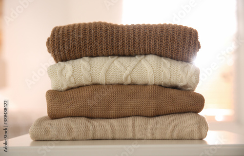 Stack of folded warm sweaters on white table indoors © New Africa
