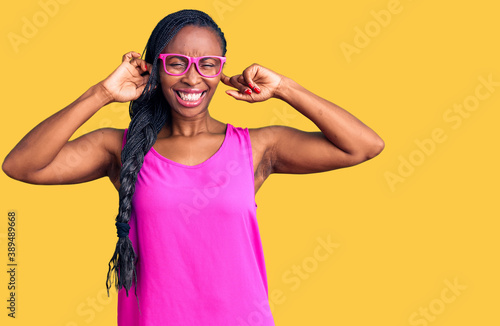 Young african american woman wearing casual clothes and glasses covering ears with fingers with annoyed expression for the noise of loud music. deaf concept.