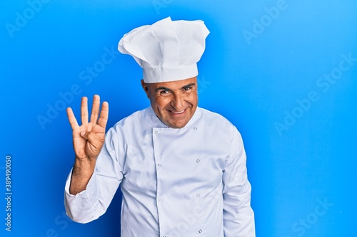 Mature middle east man wearing professional cook uniform and hat showing and pointing up with fingers number four while smiling confident and happy.