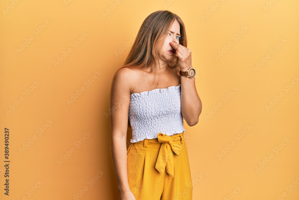 Beautiful young blonde woman wearing casual summer clothes smelling something stinky and disgusting, intolerable smell, holding breath with fingers on nose. bad smell Beautiful young blonde woman wearing casual summer clothes smelling something stinky and disgusting, intolerable smell, holding breath with fingers on nose. bad smell